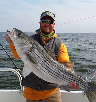 Natural Light Charter Fishing customer holding large Rockfish caught during a Chesapeake Bay charter fishing trip.