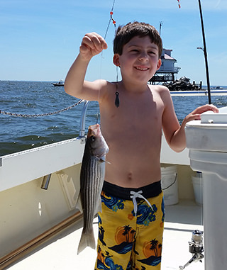 A young Natural Light Charter Fishing customer holding a small Rockfish caught during a Chesapeake Bay charter fishing trip.
